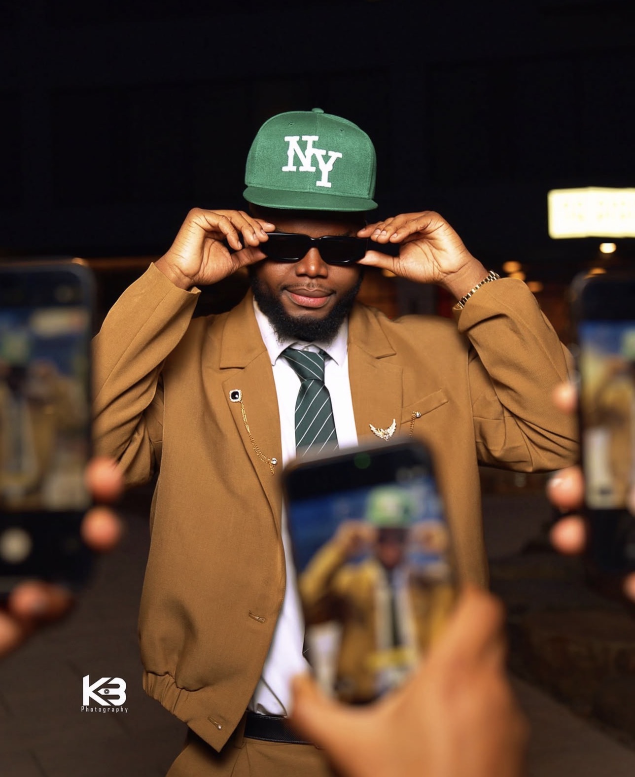 Editorial street portrait of a man in a tan suit and green cap surrounded by camera phones, creative photography by KB Photography in New York