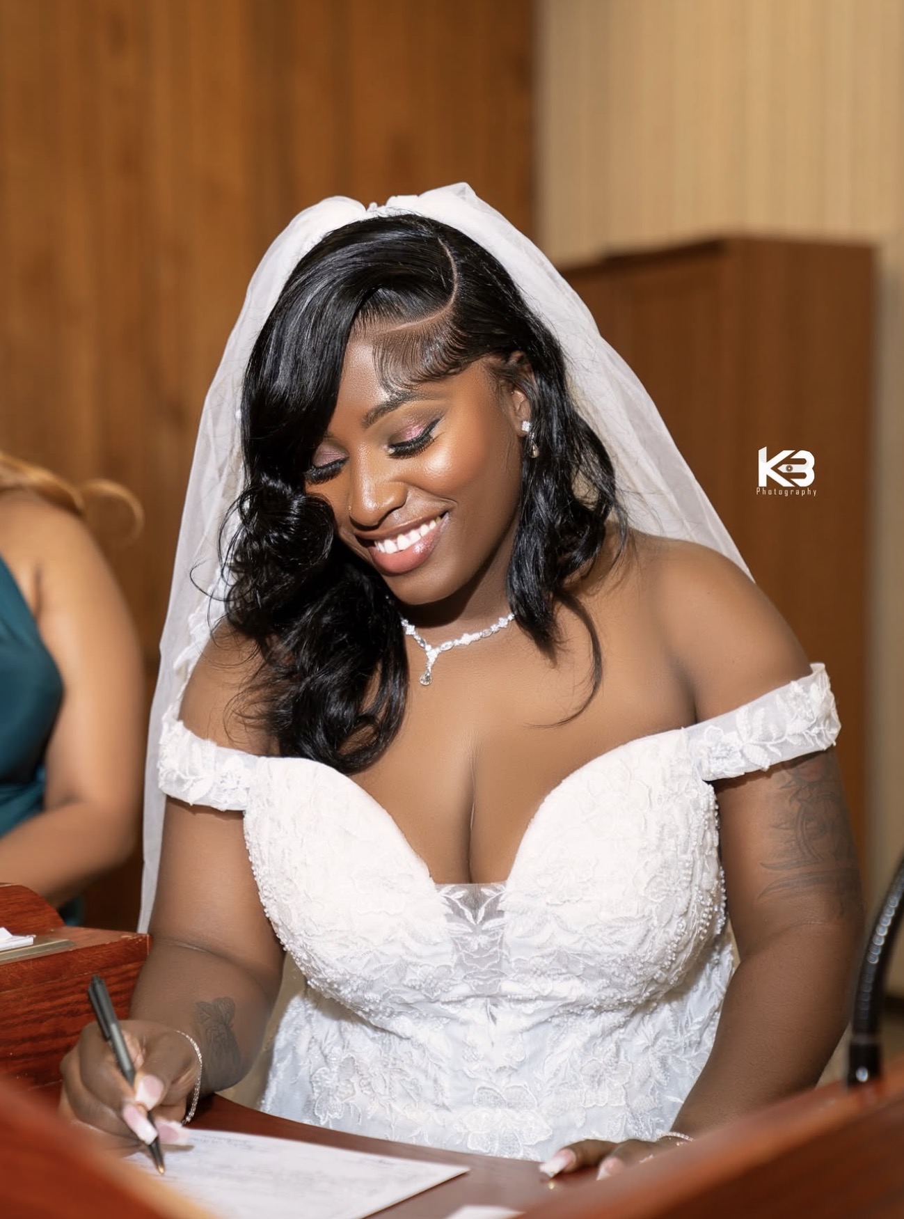 Bride in a white lace gown and veil signing her marriage certificate at a New York wedding, photographed by KB Photography